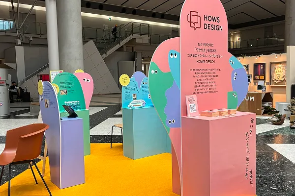 「HOWS DESIGN」と書かれたピンクやパープルのポップなパネルが並ぶ、コクヨのインクルーシブデザイン展示ブース。パネルには「違いを、気づきに。気づきを、社会に。」のキャッチコピーが記載されている。